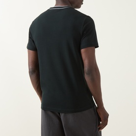 Model wearing Lacoste Crew Neck T in Dark Varech, rear view showing tipped collar detail, paired with grey trousers.