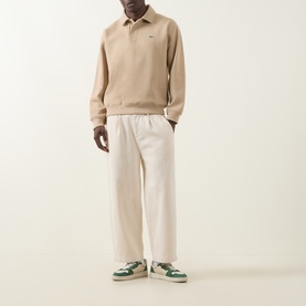 Model wearing Lacoste Viennese polo sweatshirt with cream wide-leg trousers and green and white low-top trainers.
