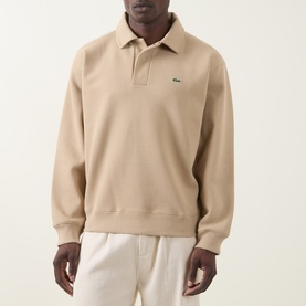 Model wearing Lacoste Viennese beige long sleeve polo sweatshirt with open collar and green crocodile logo, styled with cream trousers.