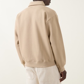 Model wearing Lacoste Polo sweat in Viennese beige, rear view, ribbed hem and cuffs, styled with white trousers