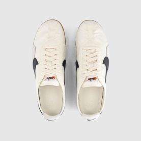 Nike Sail Black low-top trainers, overhead view showing cream suede upper, black Swoosh detail, orange branding tab and white laces.