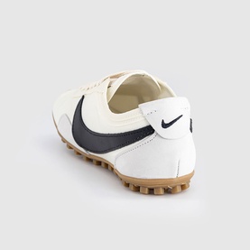 Nike trainer in sail and black with dark navy swoosh, smooth upper, and tan gum rubber sole, rear three-quarter view.