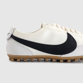 Nike trainer in sail white and black with oversized swoosh logo, lace-up front, and gum rubber sole with multi-stud traction.