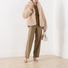 Model wearing Marella sand faux shearling coat, styled with khaki wide-leg trousers, beige heels and a small white handbag.