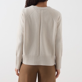Model wearing Marella turtledove wool knit jumper, back view showing ribbed hem, cuffs and raglan sleeves, styled with tan trousers.