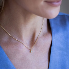 Model with Juvi March Mini Birthstone Charm Necklace in red gold, fine chain with small cubic zirconia charm pendant