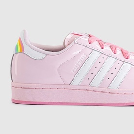 Adidas Superstar trainer in pink patent leather with white stripes, rainbow iridescent heel tab, and pink sole