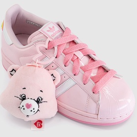 Adidas x Care Bears pink patent leather trainer with shell toe, pink laces, and Cheer Bear plush bag charm accessory.