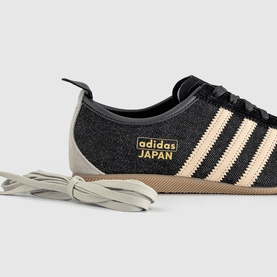Adidas Japan trainer in Core Black and Sand Strata, textile upper with cream three stripes, gold brand tab, and gum sole.