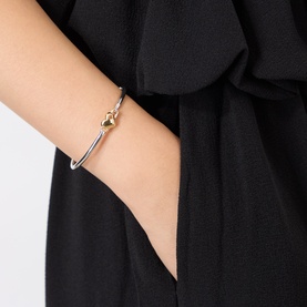 Model with Kate Spade Heart Charm Bangle in silver and gold-tone, thin curved bangle with gold heart charm detail, worn on wrist