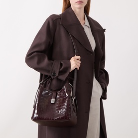 Model carrying Kate Spade crossbody bag in Blackberry Jam croc-embossed leather with gold hardware, styled with a dark brown coat.