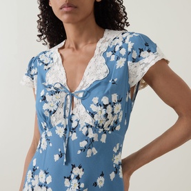 Model wearing Rixo London Bouquet Blue floral dress with white lace trim neckline and tie-front detail, cap sleeves