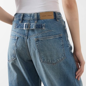 Model wearing Samsoe & Samsoe jeans in Sephia Blue, showing back pocket detail and belted waistband in 100% cotton denim.