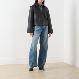 Model wearing Samsoe & Samsoe black leather jacket with wide sleeves and zip front, styled with light blue wide-leg jeans and black boots.