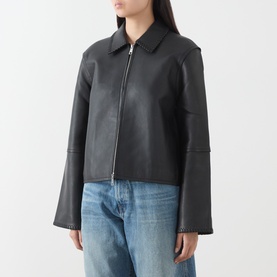Model wearing Samsoe & Samsoe black leather jacket with zip front, wide cuffs and collar, styled with blue jeans.