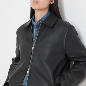 Model wearing Samsoe & Samsoe black leather jacket with zip front and pointed collar, styled over a denim shirt.