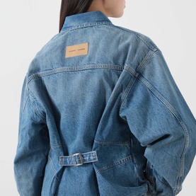 Model wearing Samsoe & Samsoe sephia blue denim shirt, back view showing oversized fit, tonal stitching, branded patch, and belted waist.