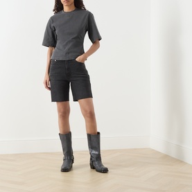 Model wearing Samsoe & Samsoe black pigment cotton T-shirt with short sleeves, styled with dark denim shorts and grey cowboy boots.