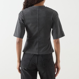 Model wearing Samsoe & Samsoe Black Pigment cotton T-shirt, back view, with seam detailing and short sleeves, styled with dark trousers.