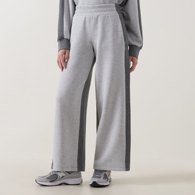 Model wearing Spanx Sweat Bottoms in light grey marl with contrast dark grey side panels, wide-leg fit, styled with grey trainers.