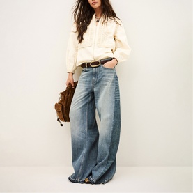 Model wearing Bash cream oversized shirt with wide-leg faded blue jeans, brown leather belt, carrying a brown suede bag.