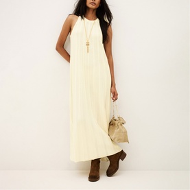 Model wearing Bash cream sleeveless maxi dress, styled with a gold pendant necklace, beige bucket bag and brown ankle boots.