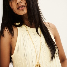 Model wearing Bash cream knitted sleeveless top with open-weave detail, styled with a long gold pendant necklace