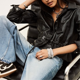 Model wearing Bash black faux leather shirt with drawstring waist, styled with blue wide-leg jeans and layered silver jewellery