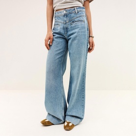 Model wearing Bash blue wide-leg jeans with diagonal zip pockets, styled with a grey crop top and gold loafers