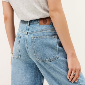 Model wearing Bash blue wide-leg jeans, rear view showing back pockets and leather patch detail, styled with a grey T-shirt.