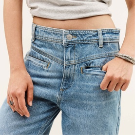 Model wearing Bash blue wide-leg jeans, close-up of waistband and front pockets, styled with a grey crop top