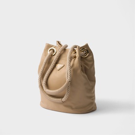Beige bucket bag with rope handles, gold-tone eyelets, and drawstring closure, small triangular logo patch on front