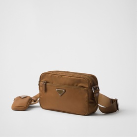 Tan nylon crossbody camera bag with silver-tone triangle logo, zip closure, adjustable strap, and small detachable pouch