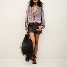 Model wearing Bash purple floral print blouse with black shorts, styled with fringe bag and strappy sandals