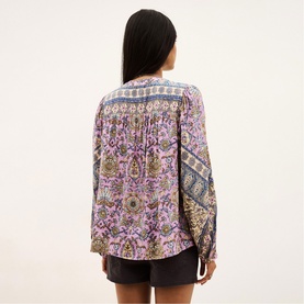 Model wearing Bash purple paisley print long-sleeve blouse, back view, styled with dark mini skirt.