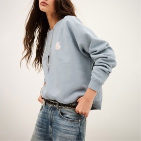 Model wearing Bash blue sweatshirt with small chest graphic, styled with denim jeans and a belt