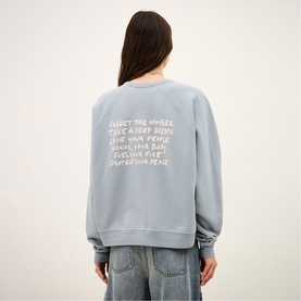 Model wearing Bash blue sweatshirt with white text print on back, styled with light wash jeans