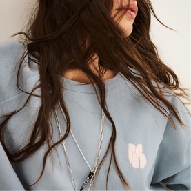Model wearing Bash blue sweatshirt with small front graphic print, styled with a layered silver chain necklace