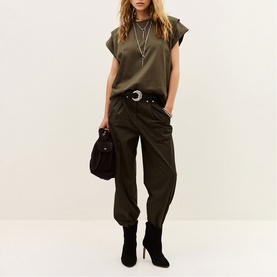 Model wearing Bash brown cargo-style trousers with khaki cap-sleeve top, crescent belt, layered necklaces, and black suede heeled boots