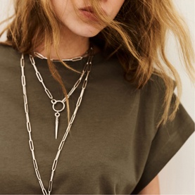 Model with Bash layered silver-tone chain necklaces featuring ring and spike pendants, styled with an olive green T-shirt