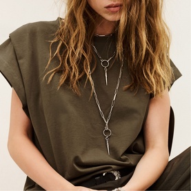 Model with layered silver chain necklaces featuring ring and spike pendants, styled with a brown sleeveless top and silver rings.
