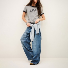 Model wearing Bash grey slogan T-shirt with black trim, styled with wide-leg blue jeans and a tied denim shirt at the waist.