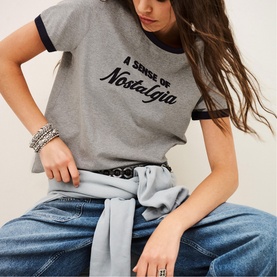Model wearing Bash grey slogan ringer T-shirt with navy trim, styled with blue jeans and a waist-tied denim shirt, silver bangles visible.
