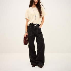 Model wearing Bash cream oversized T-shirt with wide-leg black jeans, white belt, long necklace, and carrying a small burgundy bag.