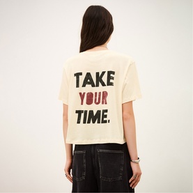 Model wearing Bash cream T-shirt, back view with bold "Take Your Time" graphic print, styled with black wide-leg trousers.