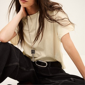 Model wearing Bash cream T-shirt with short sleeves, styled with black wide-leg trousers, belt, and layered chain necklace.