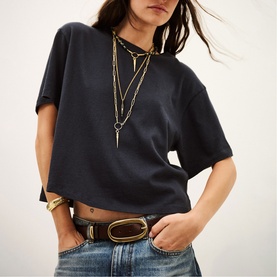 Model wearing Bash blue cropped T-shirt with layered gold necklaces, gold belt, and blue jeans.