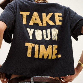 Model wearing Bash blue cropped T-shirt, back view, with gold distressed "Take Your Time" graphic print.