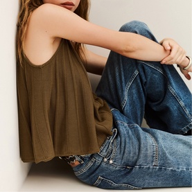 Model wearing Bash brown sleeveless swing top with relaxed blue denim jeans, seated against a white wall.