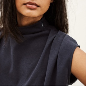 Model wearing Bash blue sleeveless high-neck top with draped front detail and cap sleeves, close-up view